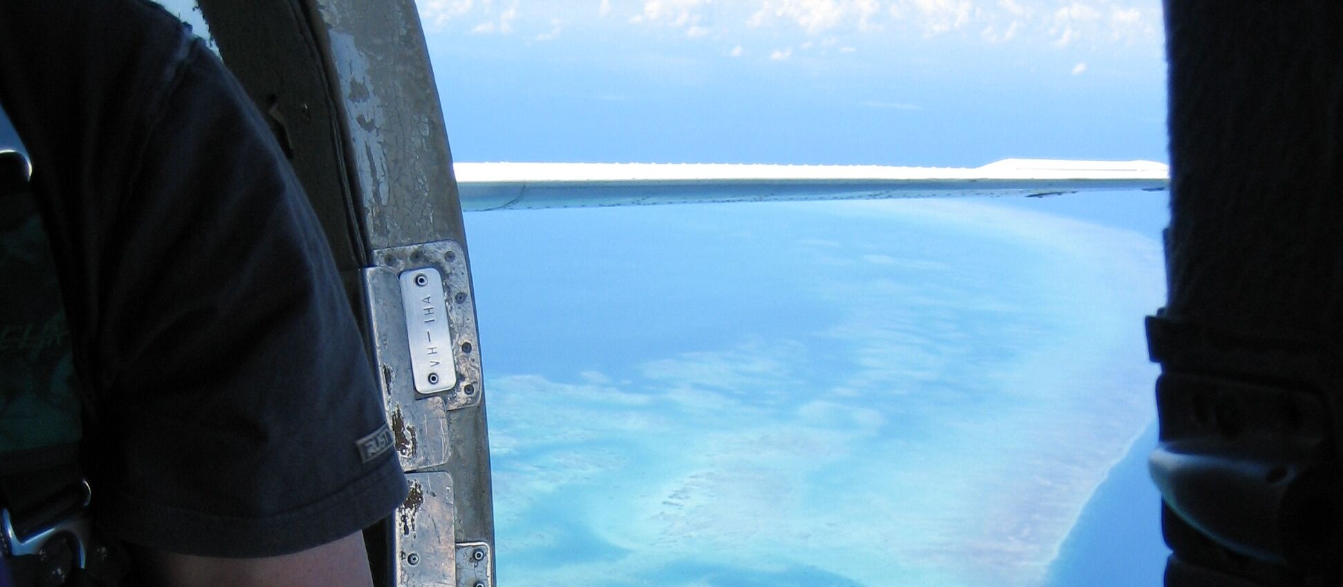 The view from an open aircraft door: the wing, the horizon, and a reef far below